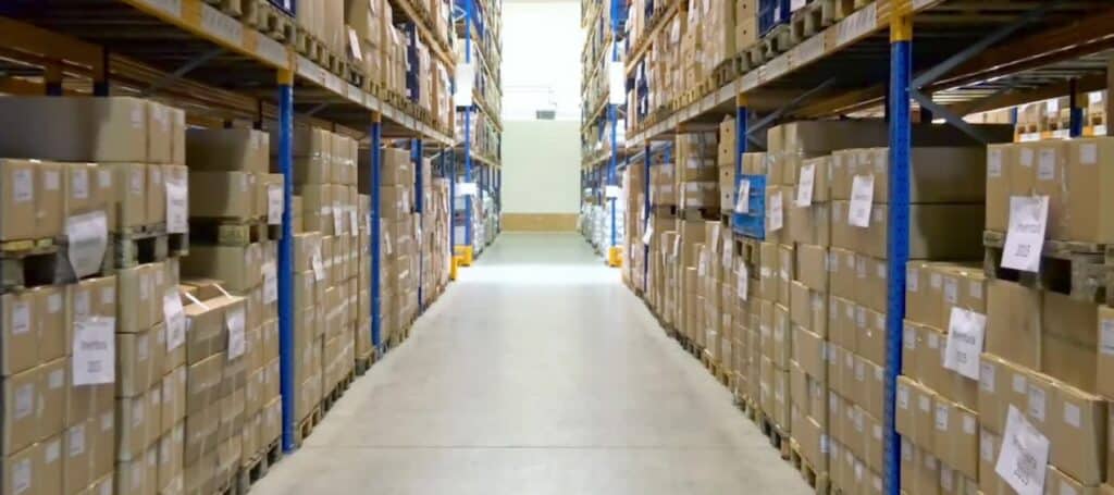 Großes Warenlager mit hohen Regalen voller Kartons – Blick entlang eines Logistikgangs